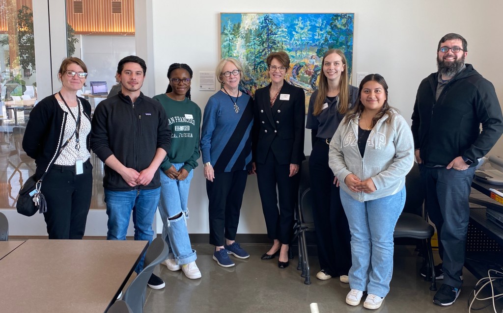 Eight people pose for a photo in a classroom