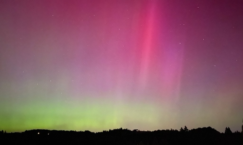 A dark silhouette of a mountain range spreads across the bottom of the photo. Green and Pink colors of the Aurora Borealis fill the sky